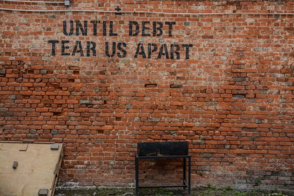 A close‑up photograph of brick wall displaying the words "until debt tear us apart"; the image conveys the seriousness and administrative tone associated with managing tax debt obligations in New Zealand.